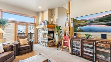 A cozy living room with a fireplace, a comfortable leather sofa, a television, and a scenic painting on the wall.