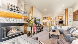 Een ruime woonkamer met een open haard, een zithoek en een keuken op de achtergrond.