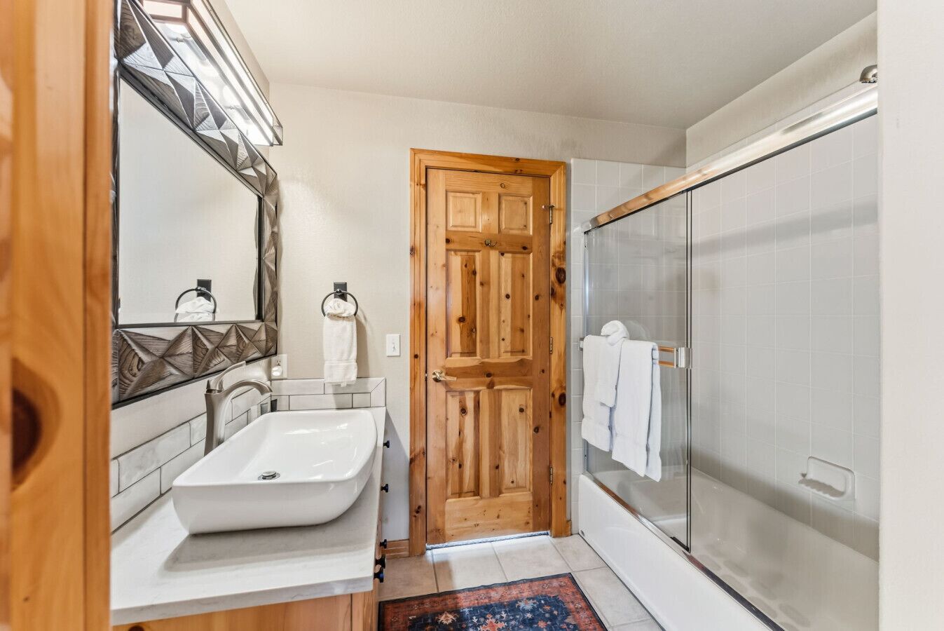 A bathroom with a large sink, a wooden door, and a glass shower enclosure.