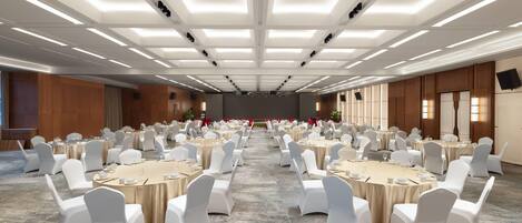 A large conference room with multiple round tables and white chairs, equipped with microphones and screens.