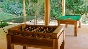 A pool table, a foosball table, and a ping pong table in an outdoor setting with greenery in the background. - Pousada Roca (Ibiúna)