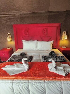 A hotel room with a red headboard, white bedding, and two wall-mounted light fixtures. - Merzouga white camp  (Merzouga)