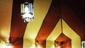 A hotel room with a vaulted ceiling, three beds with orange bedding, white headboards, and a chandelier. - Merzouga white camp  (Merzouga)