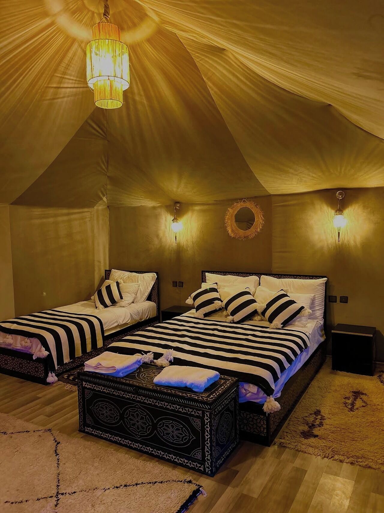 A tent-style bedroom with two beds, a decorative wall hanging, and a hanging light fixture.