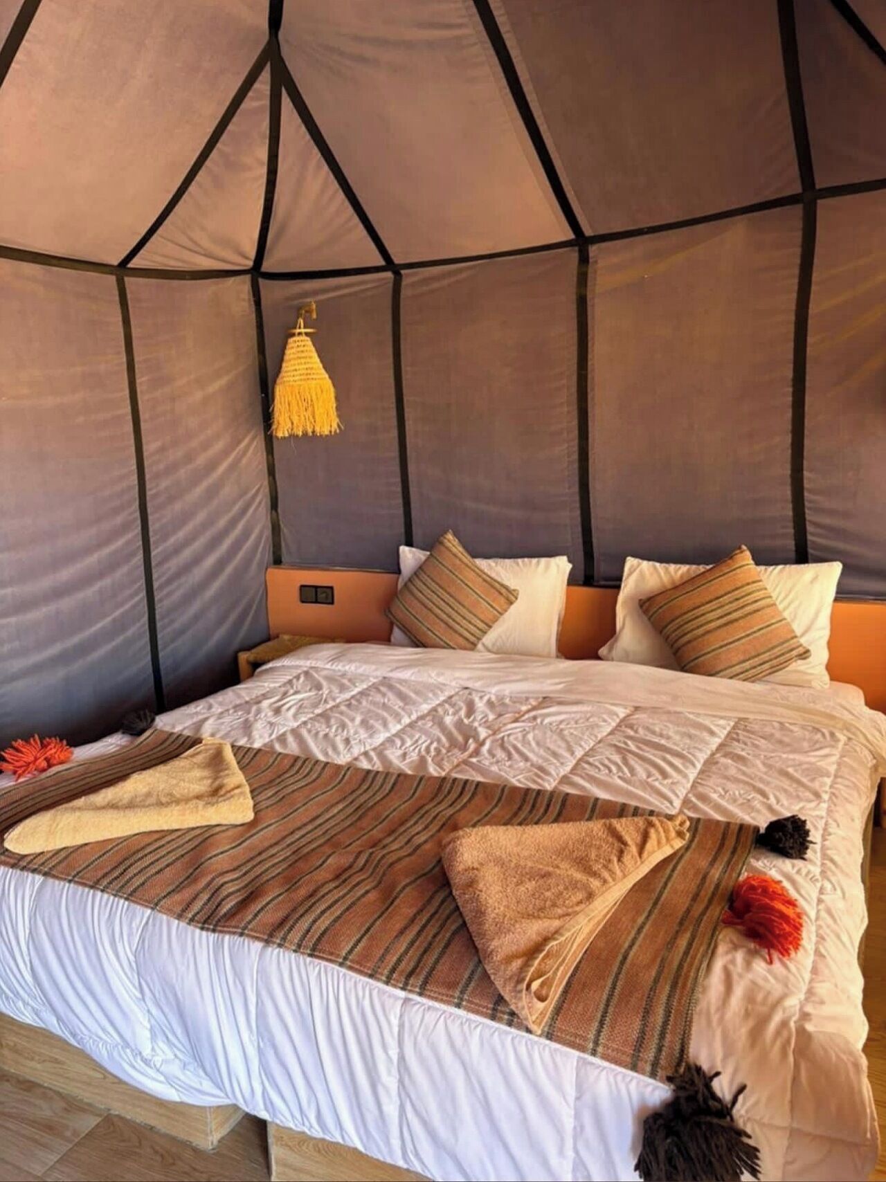 A bed with a striped blanket, pillows, and a hanging lamp in a tent-like room.