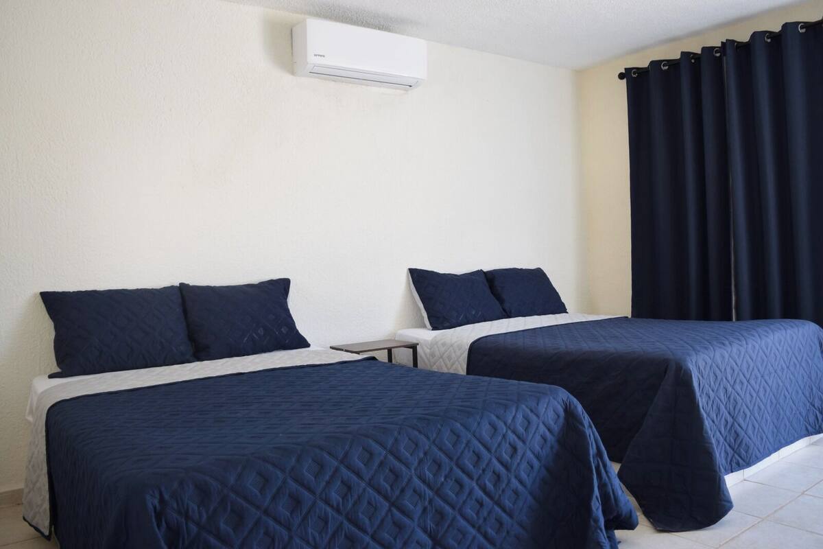 Une chambre d’hôtel avec deux lits, une petite table et une fenêtre avec des rideaux foncés.