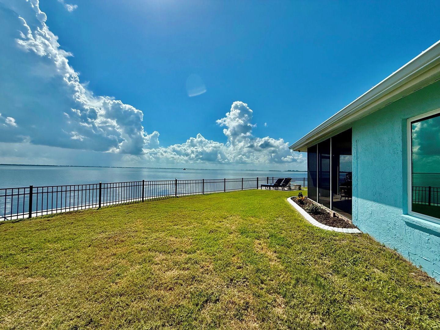 A house with a view of a body of water, a fenced yard, and a clear sky.