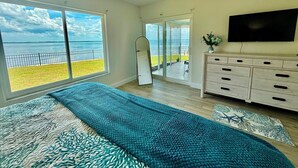 Een slaapkamer met een groot bed, een televisie en uitzicht op zee door de ramen.
