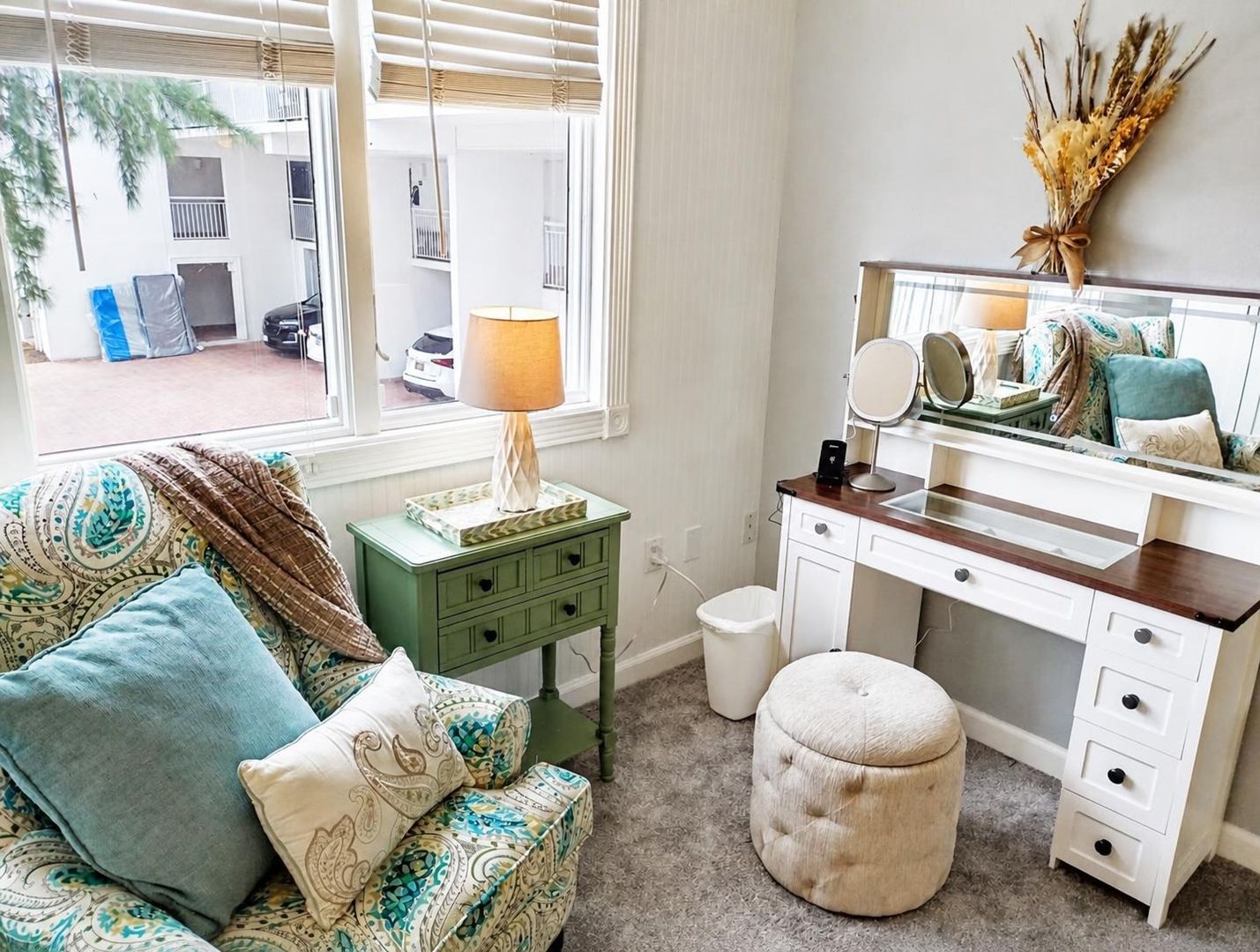 A bedroom with a bed, a dresser, a vanity with a mirror, and a window with blinds.
