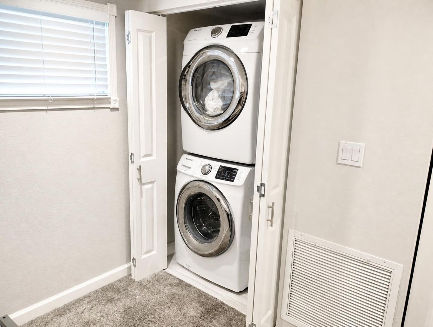 Une buanderie équipée de deux machines à laver et deux sèche-linge superposés, une porte et une bouche d’aération.