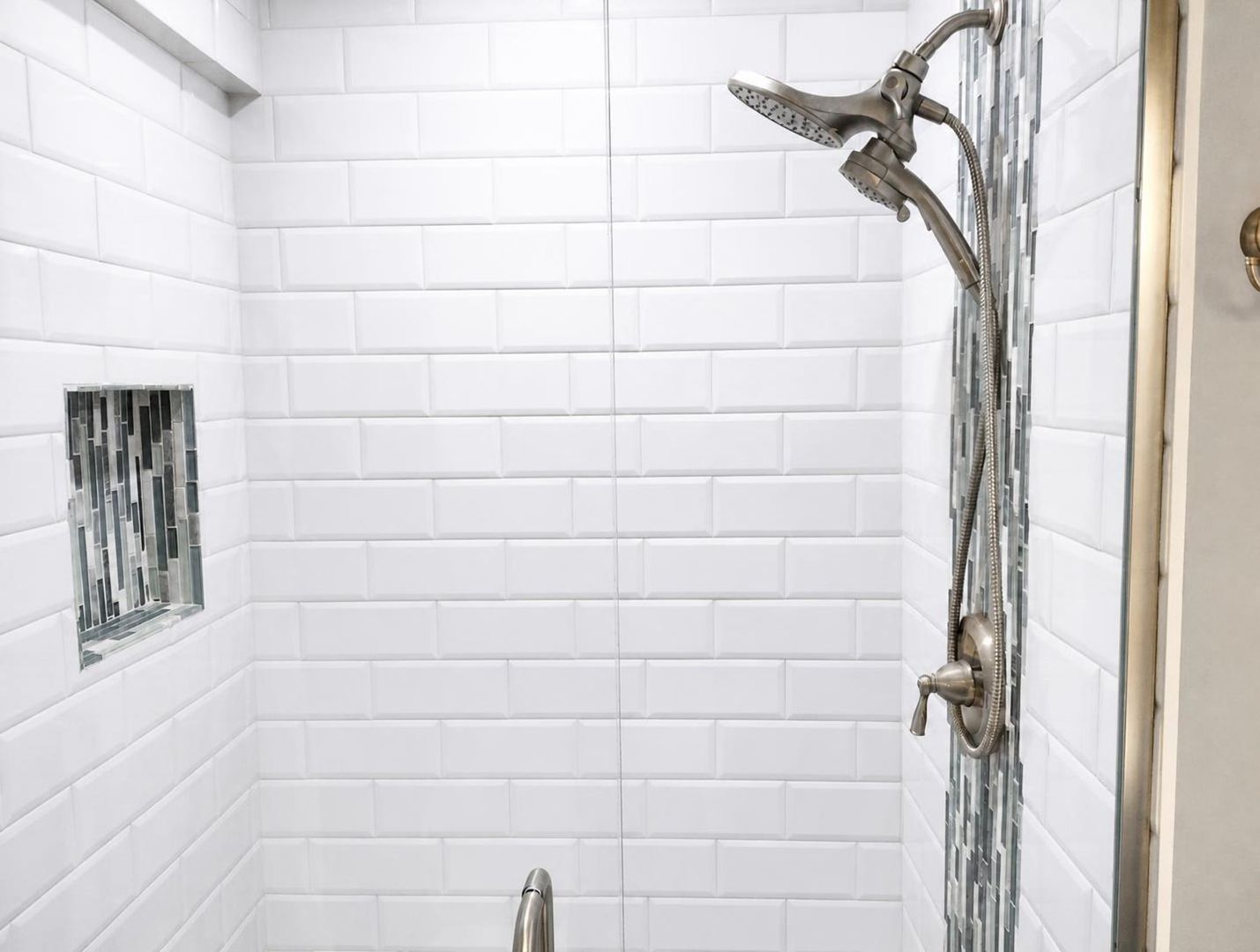 A bathroom with white subway tiles, a shower with a handheld showerhead, and a small window with a metal grille.