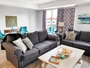 A modern living room with two grey sofas, a coffee table, and a balcony with patterned curtains. - Gorgeous 3-bedroom beachfront unit at Club Longboat! (Longboat Key)