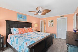 Ein Schlafzimmer mit einem Bett, Deckenventilator, Nachttisch, Lampe, Kommode und einer Tür.