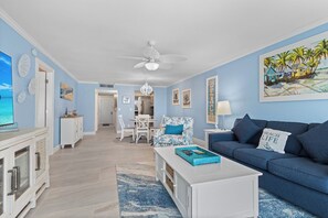 Ein Wohnzimmer mit einem blauen Sofa, einem weißen Couchtisch und einem Essbereich mit einem weißen Tisch und Stühlen.