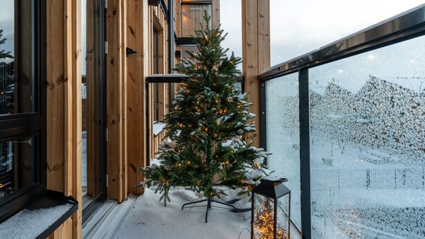 A wooden-framed balcony with a snow-covered ground, a Christmas tree with lights, and a view of a snowy landscape through a window. - Le Chalet Lingonberry D7 by Aavalevi (Levi)