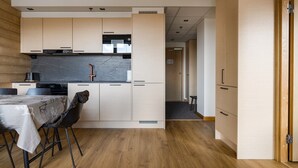 A modern kitchen with wooden cabinets, a black countertop, and a dining area with a table and chairs. - Le Chalet Lingonberry D7 by Aavalevi (Levi)