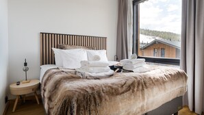 A bedroom with a bed, a bedside table, a lamp, and a window with a view of a building. - Le Chalet Lingonberry D7 by Aavalevi (Levi)