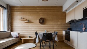 A modern kitchen with wooden cabinetry, a dining area with a table and chairs, and a sofa with a view of the outdoors. - Le Chalet Lingonberry D7 by Aavalevi (Levi)