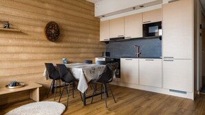 A modern kitchen with wooden walls, a dining table with chairs, and a microwave. - Le Chalet Lingonberry D7 by Aavalevi (Levi)