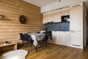 A modern kitchen with wooden walls, a dining table with chairs, and a microwave. - Le Chalet Lingonberry D7 by Aavalevi (Levi)