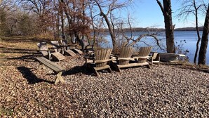 Un espace de détente aménagé au bord du lac, avec des chaises en bois et un banc, entouré d’arbres et offrant une vue dégagée sur le lac.