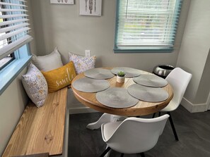 A dining area with a round wooden table, white chairs, and a bench with decorative pillows. - Trendy neighborhood, walkable to local restaurants and shops, near OSU (Columbus)