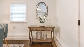 Una consola de madera con un espejo, dos cestas de alambre y una planta en maceta con flores blancas.