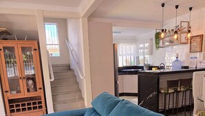 Uma sala de estar moderna com um sofá azul, um armário de madeira com portas de vidro e uma escada que dá acesso a uma área de cozinha.