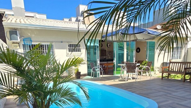Piscina com deck revestido, cercada por plantas em vasos e mobiliário de exterior.