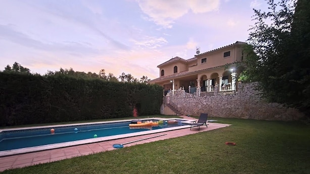 A swimming pool with a stone wall and a grassy area in front.