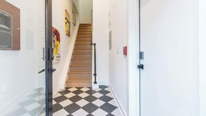 A hallway with a checkered floor, a staircase, and a door with a red emergency exit sign. - Luxury Old City - The Heritage (Philadelphia)