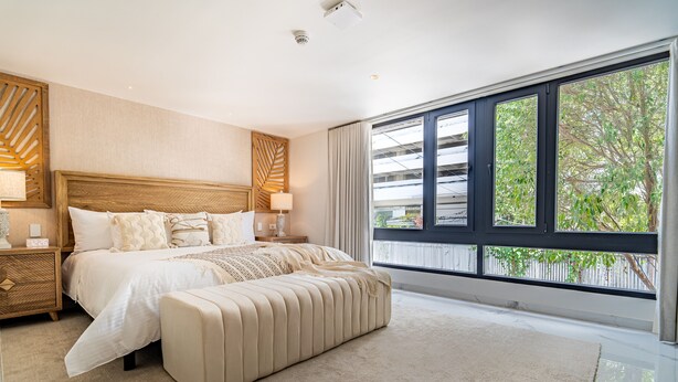 A modern bedroom with a large bed, a nightstand, a bench, and a large window with a view of greenery. - Berthas Collection By EM Hotels (Cartagena)