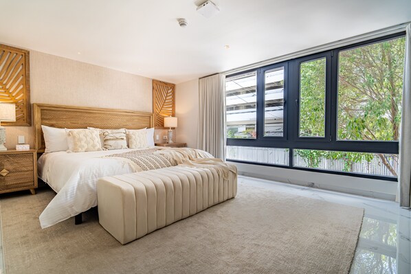 A modern bedroom with a large bed, a nightstand, a bench, and a large window with a view of greenery. - Berthas Collection By EM Hotels (Cartagena)