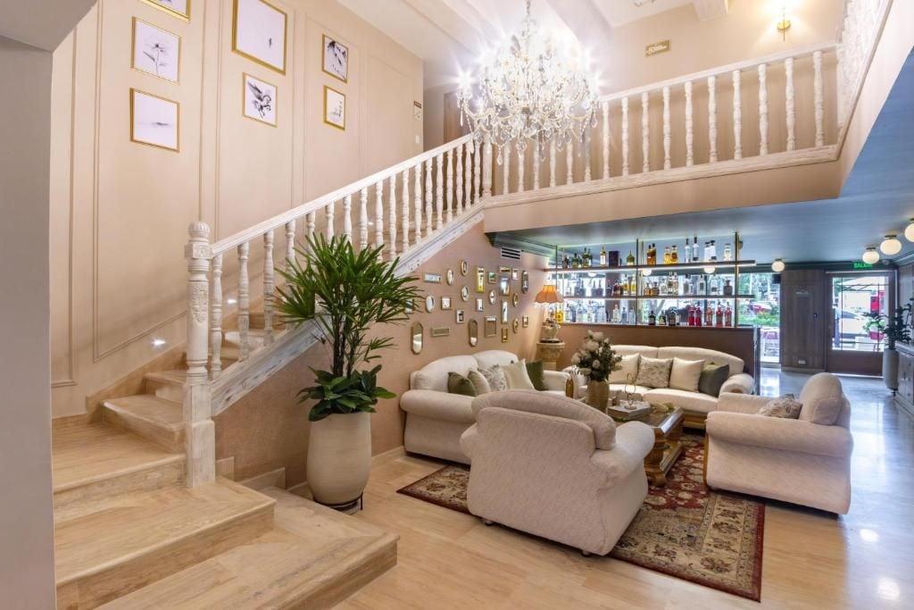 A spacious living area with a staircase, a chandelier, and a bar area with various bottles.