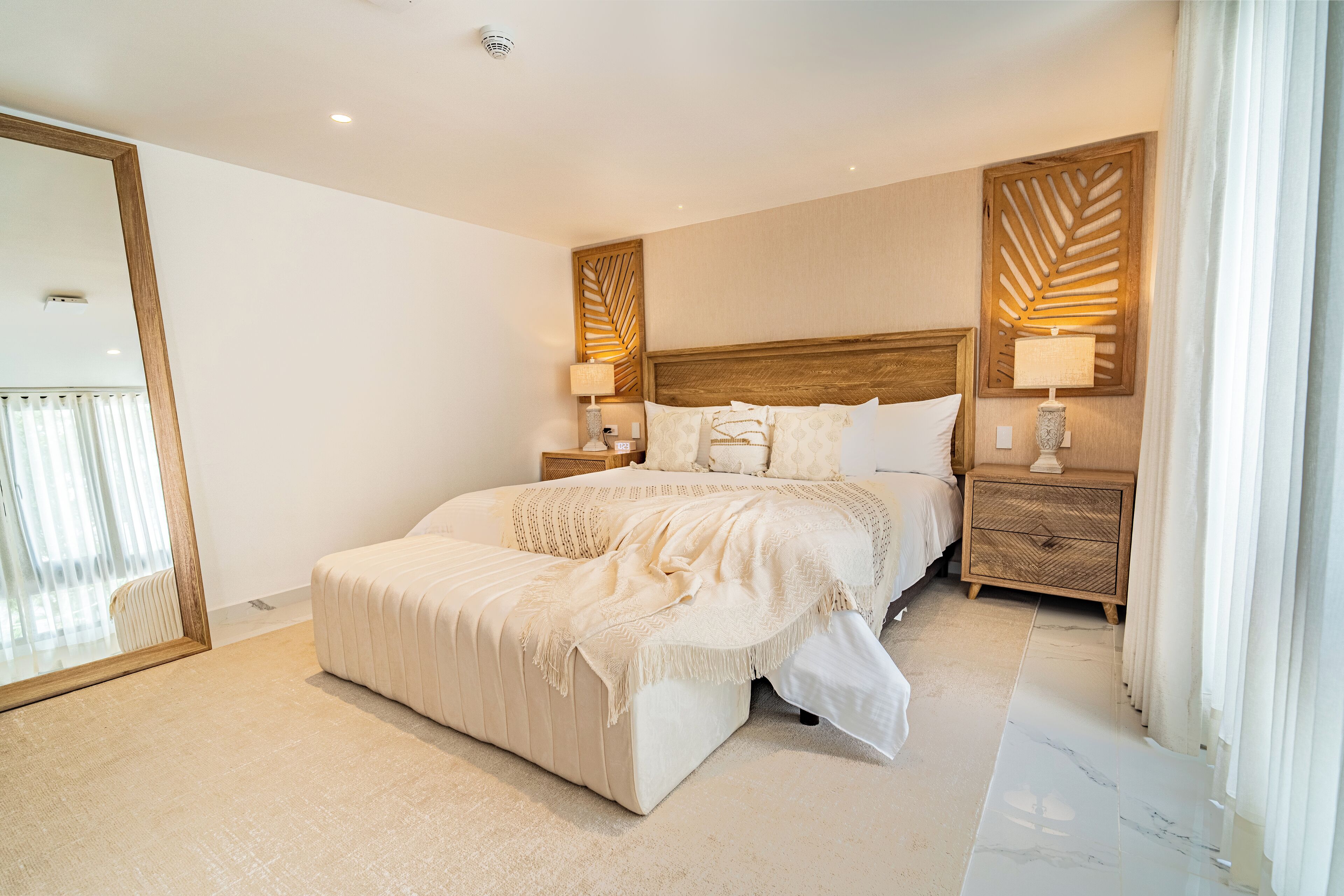 Um quarto espaçoso com uma cama grande, duas mesas de cabeceira, uma cabeceira de madeira e um espelho.