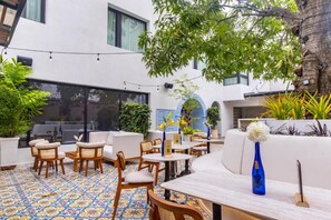 An outdoor seating area with tables and chairs, surrounded by potted plants and a tree. - Berthas Collection By EM Hotels (Cartagena)