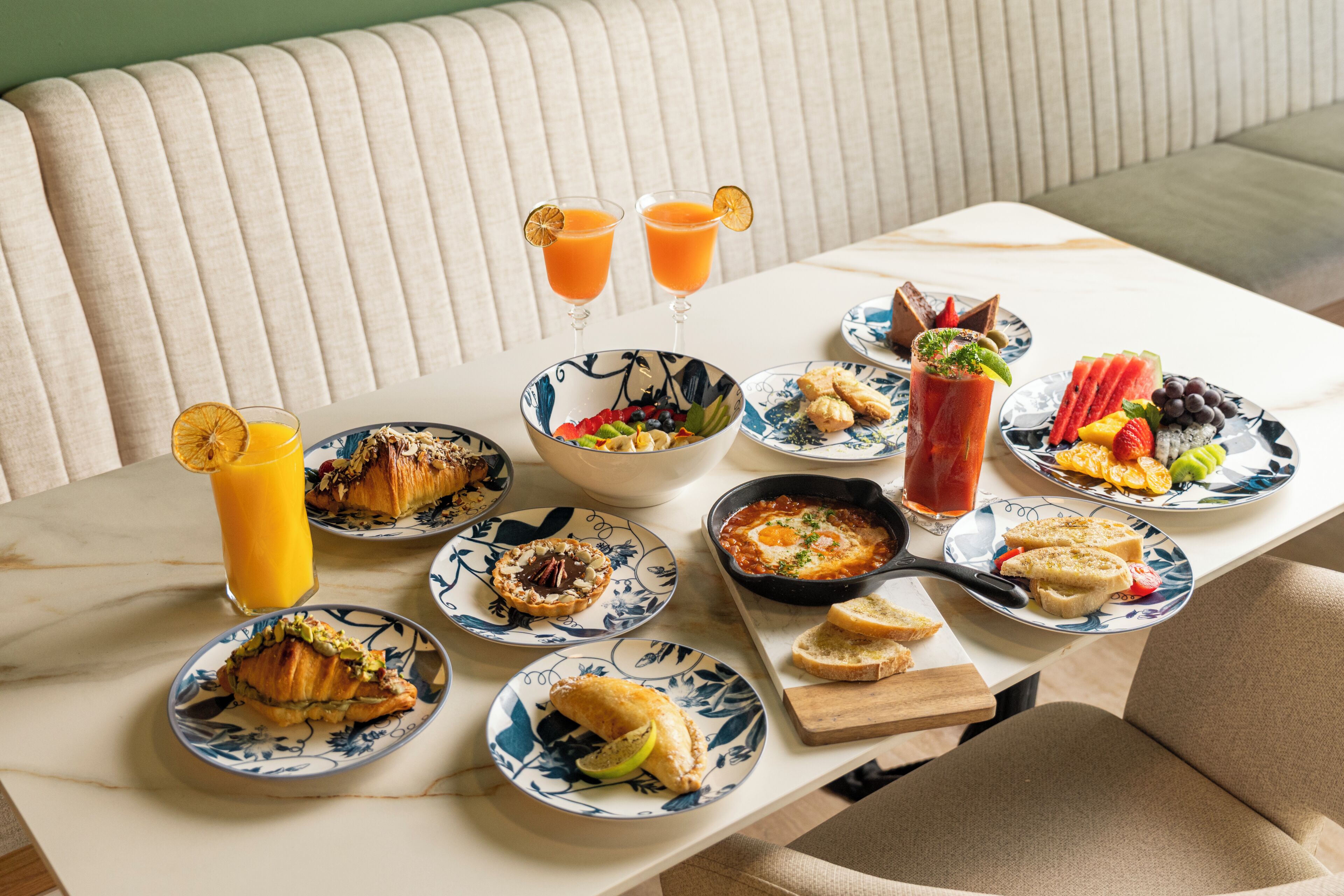 A dining table with various breakfast dishes, drinks, and a bowl of fruit.