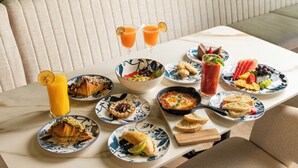A dining table with various breakfast dishes, drinks, and a bowl of fruit. - Berthas Collection By EM Hotels (Cartagena)