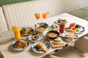 A dining table with various breakfast dishes, drinks, and a bowl of fruit. - Berthas Collection By EM Hotels (Cartagena)
