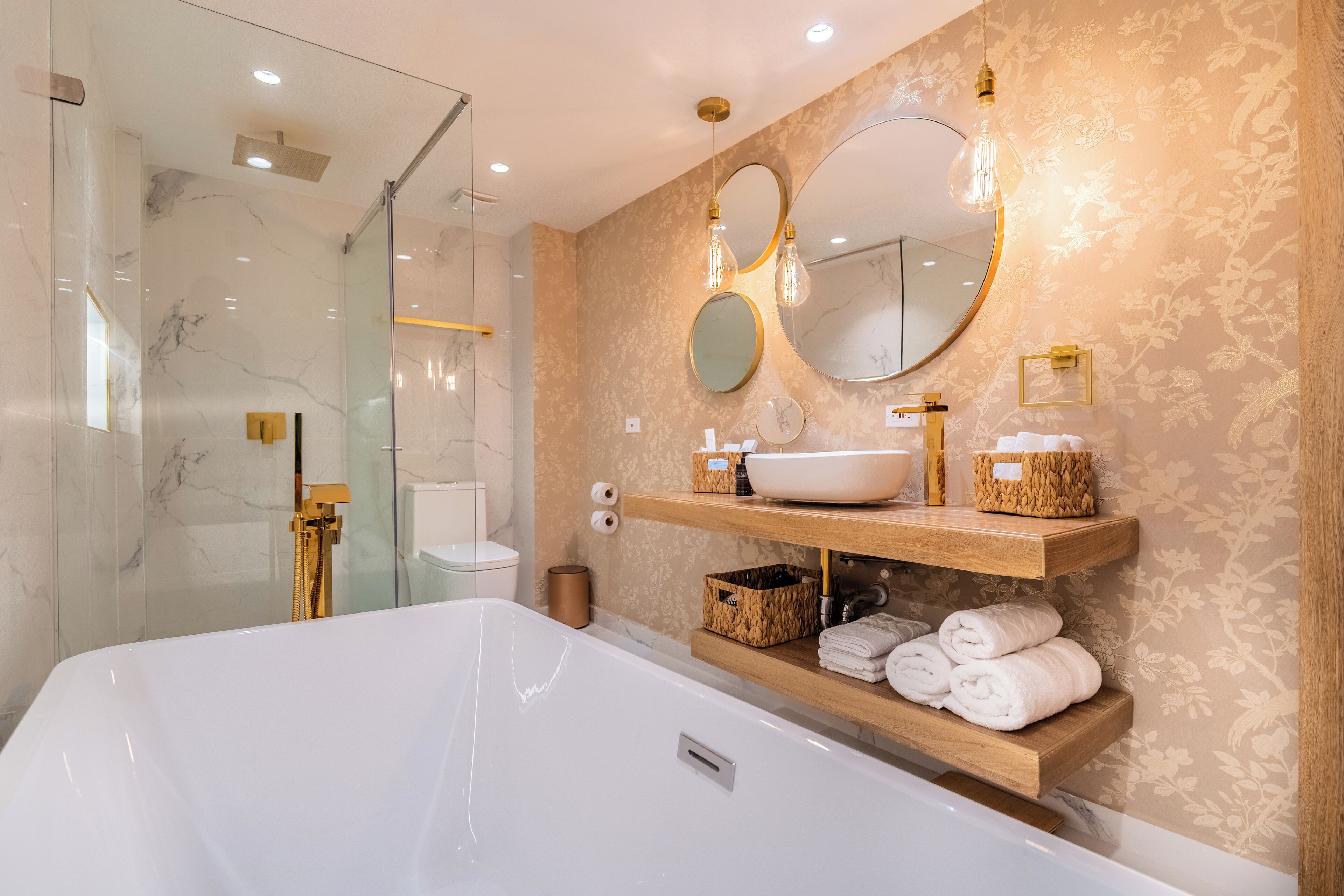 Un baño moderno con una bañera blanca grande, cabina de ducha de vidrio y estantes de madera con artículos de aseo.