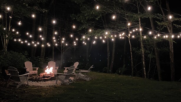 A nighttime outdoor seating area with string lights, a fire pit, and Adirondack chairs. - Cozy Boone Cabin, Fireplace, Views, 9 Min to Town (Boone)