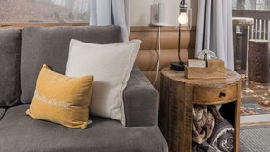 A living room with a grey sofa, a wooden side table, a clock, and a view of trees through a window. - Cozy Boone Cabin, Fireplace, Views, 9 Min to Town (Boone)