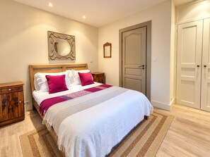 Ein Schlafzimmer mit einem Bett, einem Holz-Kopfstück, zwei Nachttischen, einem Spiegel, einer Tür und einem Kleiderschrank.