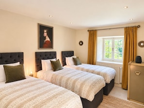 A hotel room with two beds, a window with curtains, a radiator, and a painting on the wall.