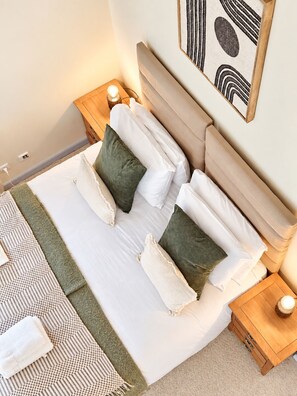 A neatly made bed with pillows and a blanket, wooden nightstands with lamps, and a wall-mounted artwork.