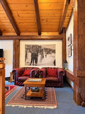 Ein gemütliches Wohnzimmer mit Holzbalkendecke, einem roten Ledersofa, einem Couchtisch und einem großen Schwarz-Weiß-Foto an der Wand.