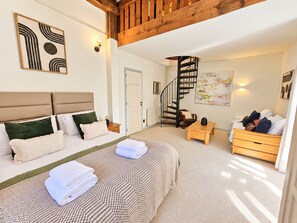 A bedroom with a bed, a wooden headboard, a wall-mounted artwork, a staircase, and a small table.