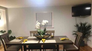 Un'area pranzo con un tavolo di legno, sedie, una panca, un centrotavola con fiori e una TV montata a parete.