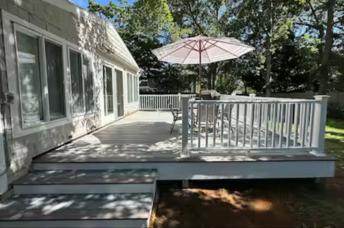 Une terrasse dotée d’une balustrade blanche, d’un parasol et d’un petit espace aménagé pour s’asseoir à l’extérieur.
