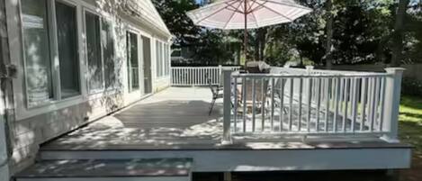 Une terrasse dotée d’une balustrade blanche, d’un parasol et d’un petit espace aménagé pour s’asseoir à l’extérieur.